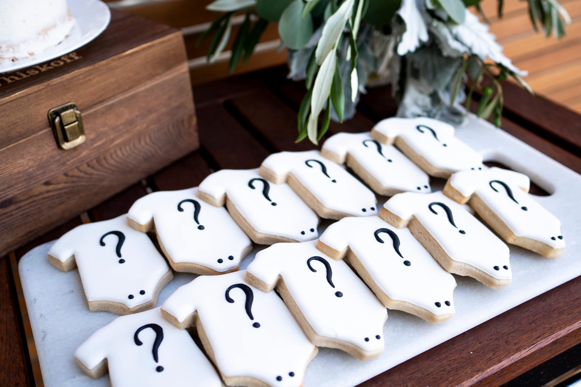 white baby onesie sugar cookies with black question marks stacked on a marble serving platter.